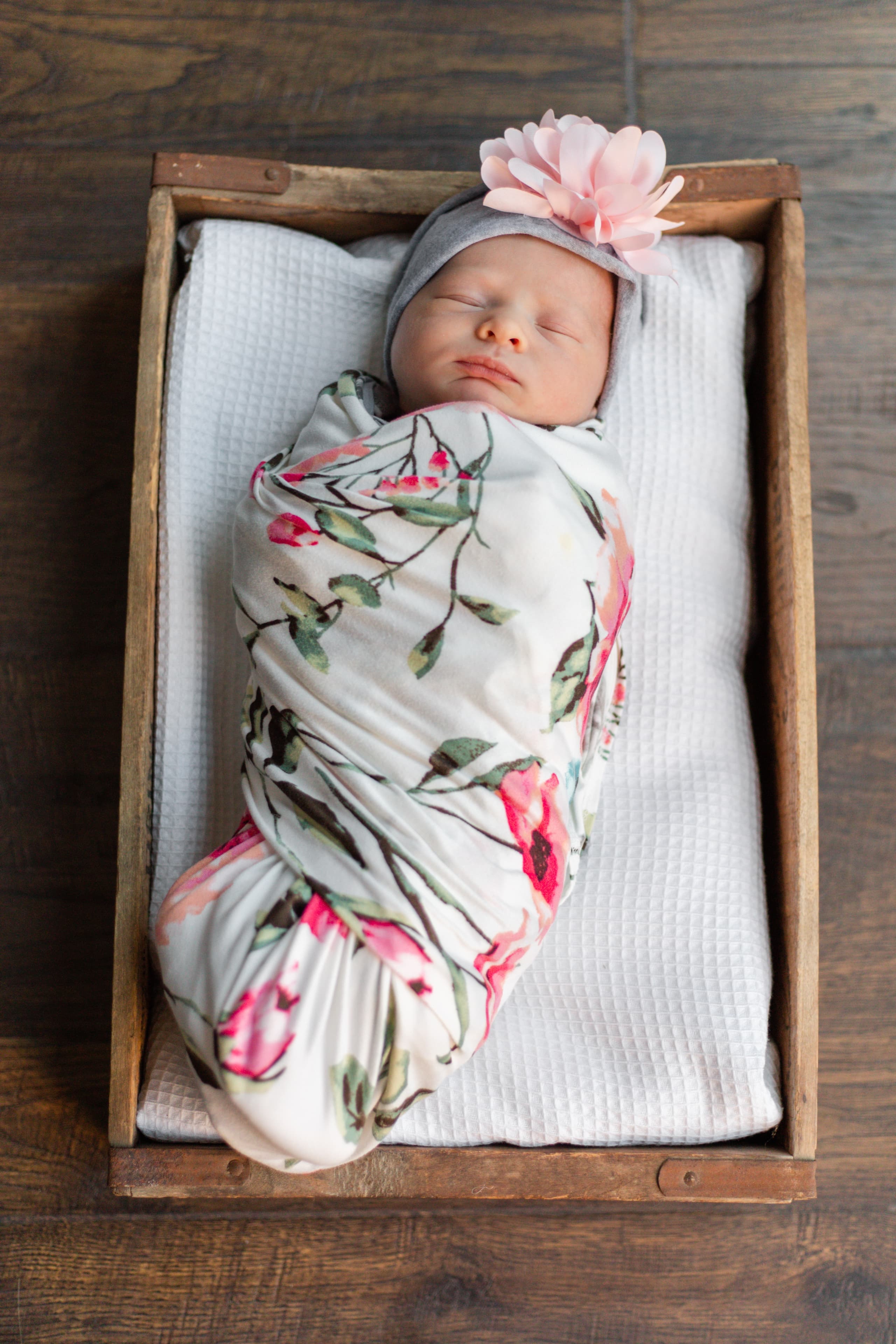 Newborn swaddled in florals, nestled in a wooden crate